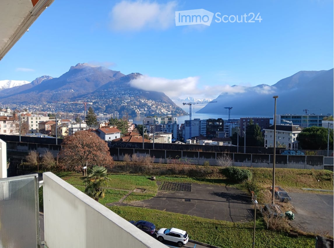balcony view, city view, parking lot, greenery, cars parked