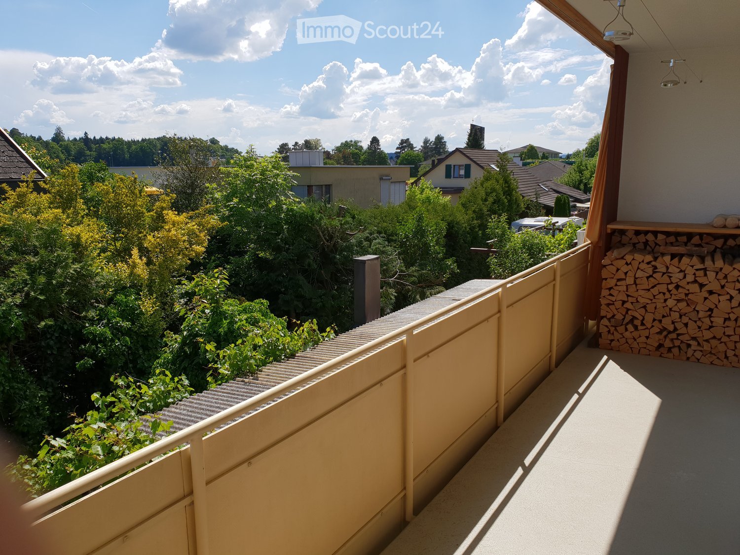 Wooden balcony with a view of the surrounding neighborhood, including houses, trees, and a cloudy sky.