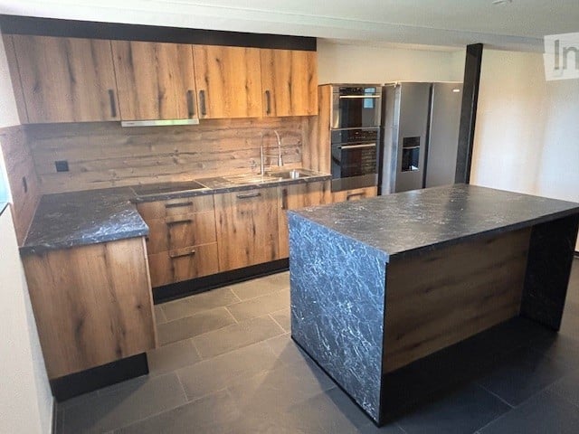 Modern kitchen with wood cabinets, stone countertops, and stainless steel appliances including a dishwasher.