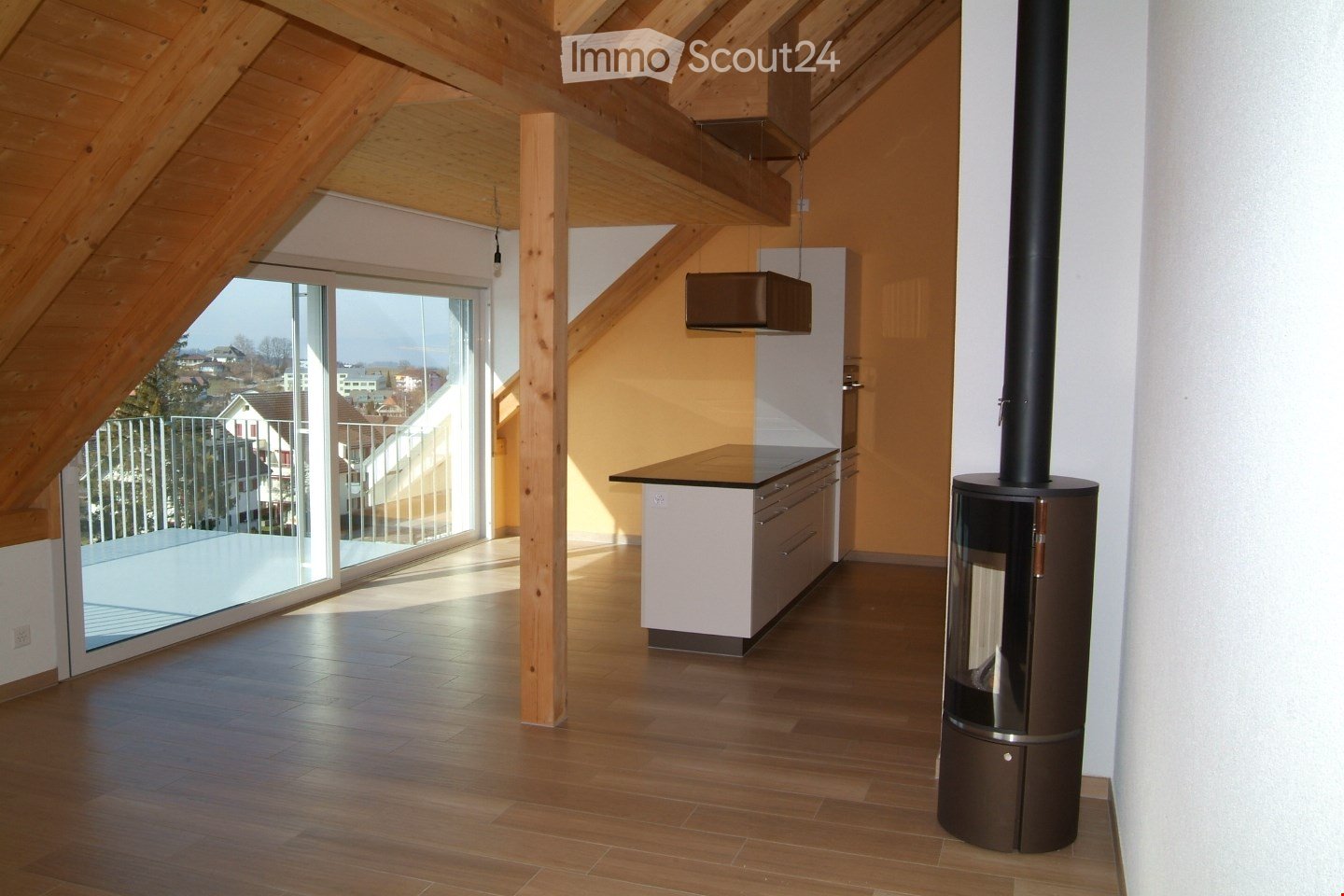 Open-concept living space with wooden beams, large windows, balcony, and a fireplace