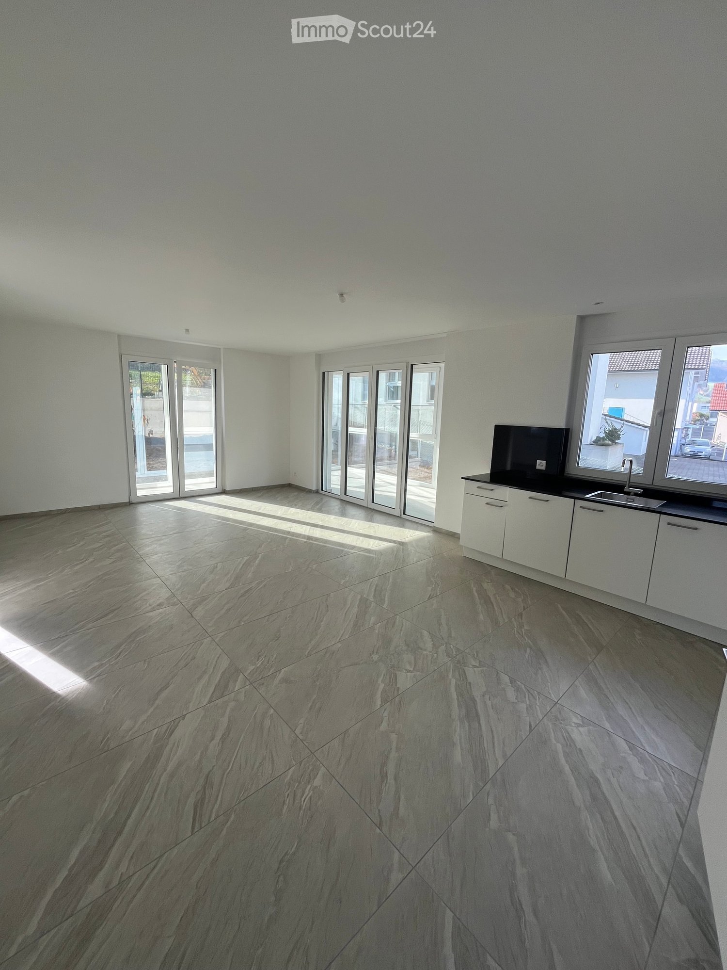 Open-plan kitchen and living room with sliding glass doors, gray tile floor, white kitchen cabinets, black countertops, modern sink with faucet