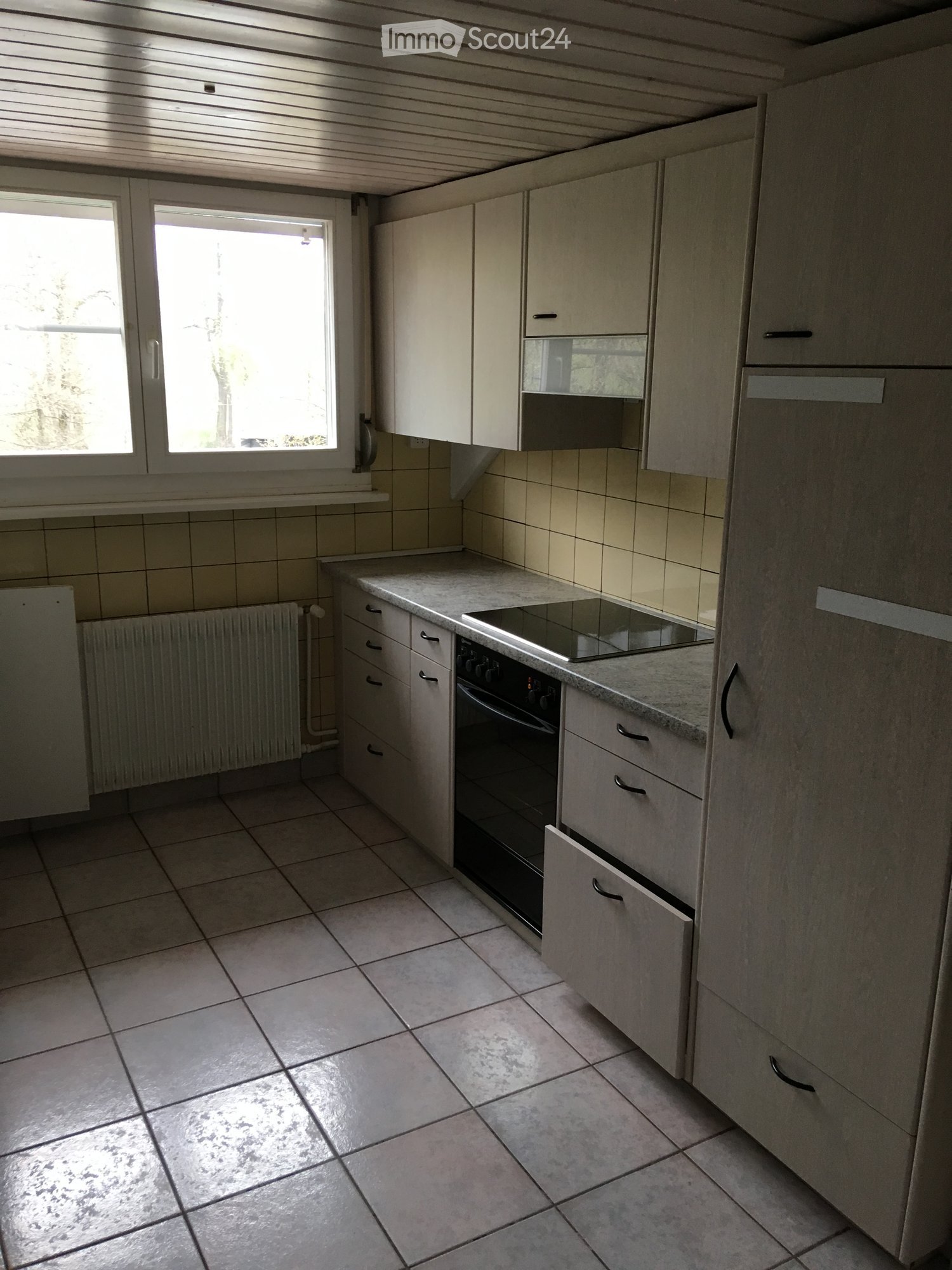 Empty kitchen, tiled floor, white cabinets, electric stove, oven, yellow tiled walls, gas radiator, countertop with stove