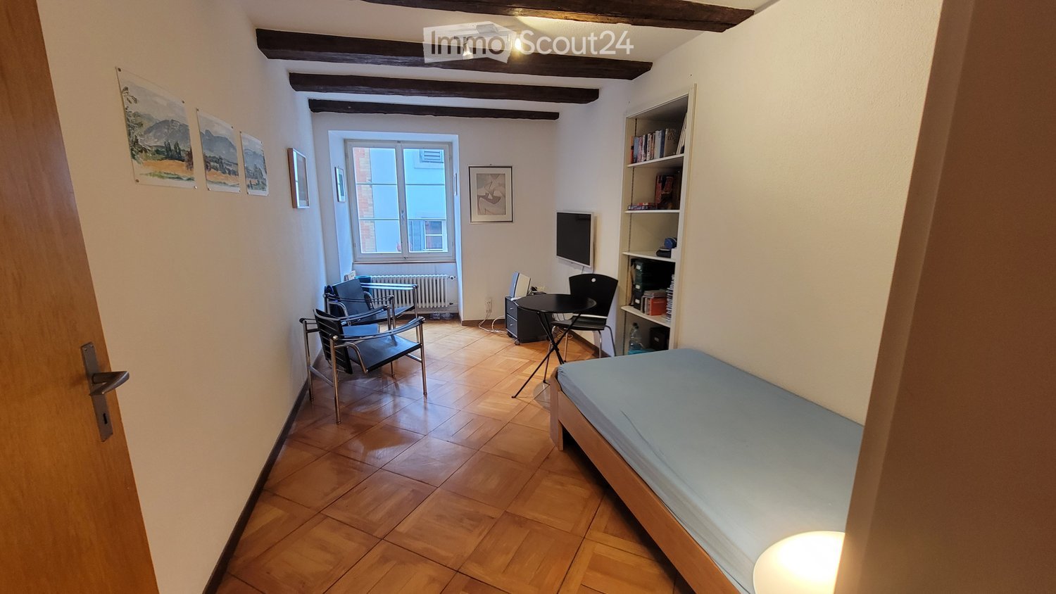 Wooden floor, white walls, single bed, small desk, chair, radiator, mounted TV, wooden beams on ceiling, framed pictures, lamps on ceiling