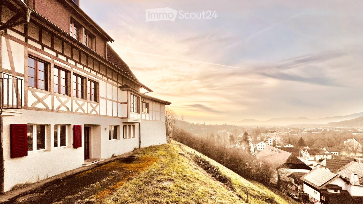 White exterior, red shutters, positioned on hill, distant town and mountains in background, green yard in front, cloudy sky