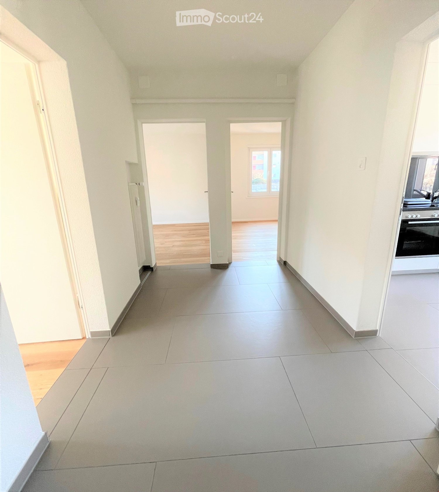 Empty hallway with tiled flooring, white walls, and wooden flooring in one room.