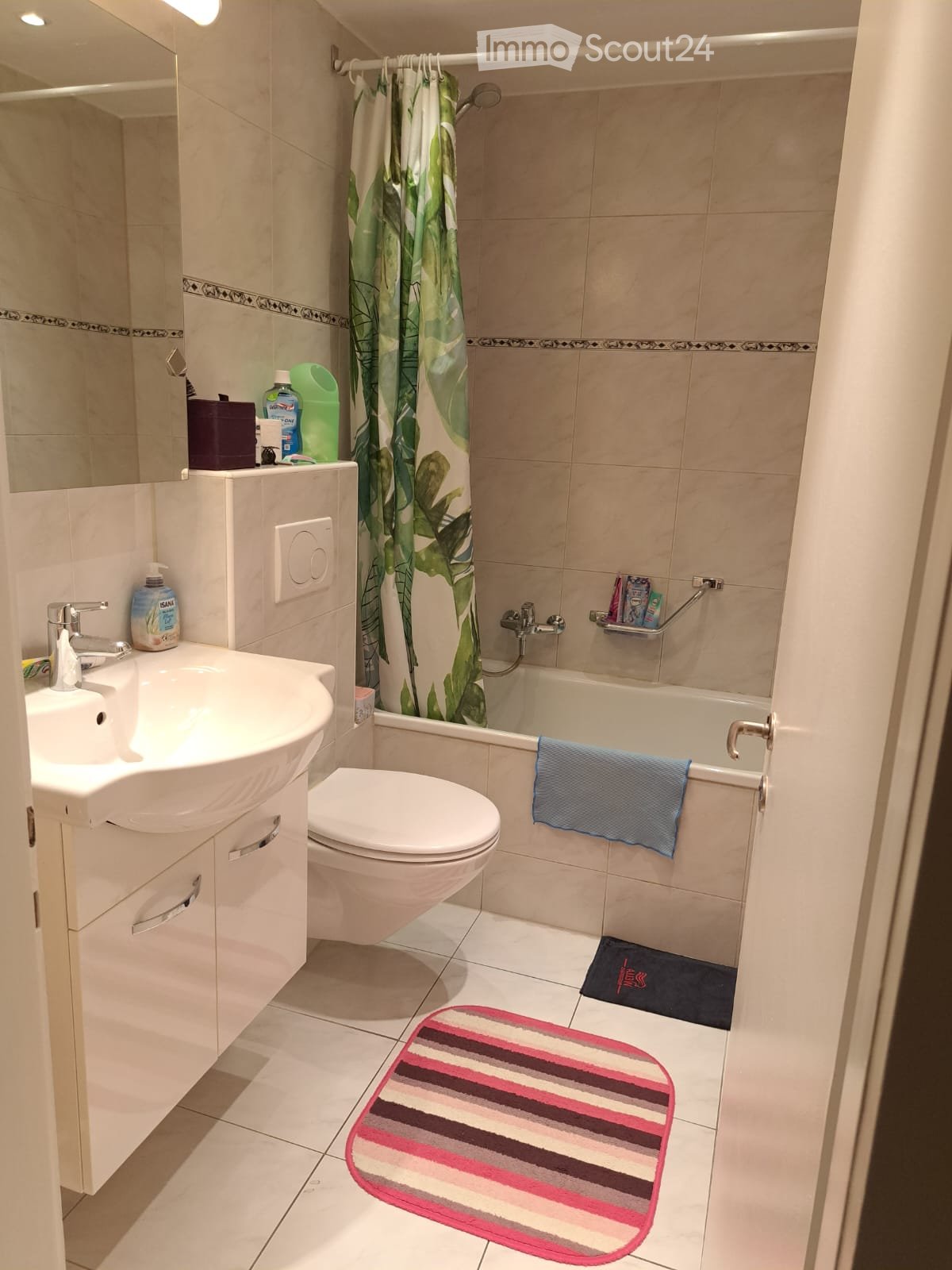 white tile, white porcelain sink, white toilet, shower with curtain, mirror, towel, bathtub, toiletries, rug, faucet, soap dispenser