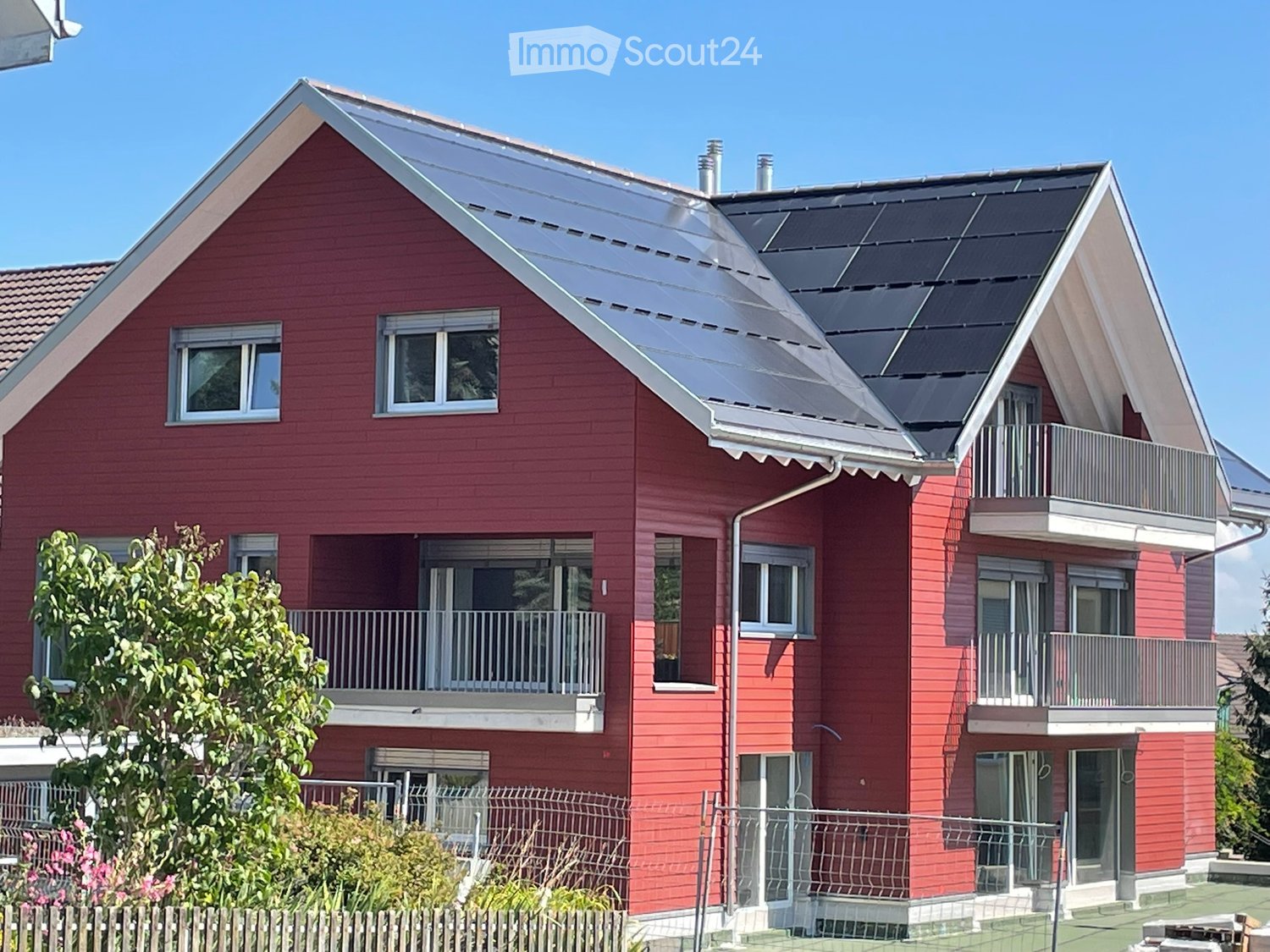 Modern red house with solar panels, two stories, multiple balconies, green lawn