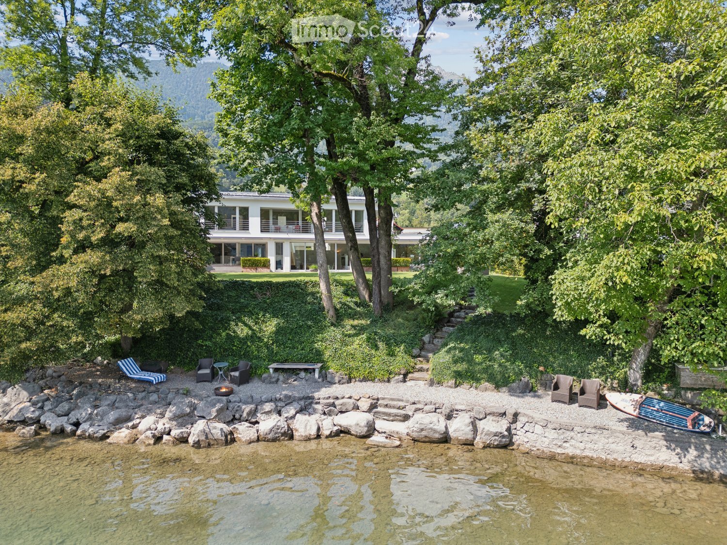 Lakeside house, white walls, multiple windows, wooden seating, fire pit, boat