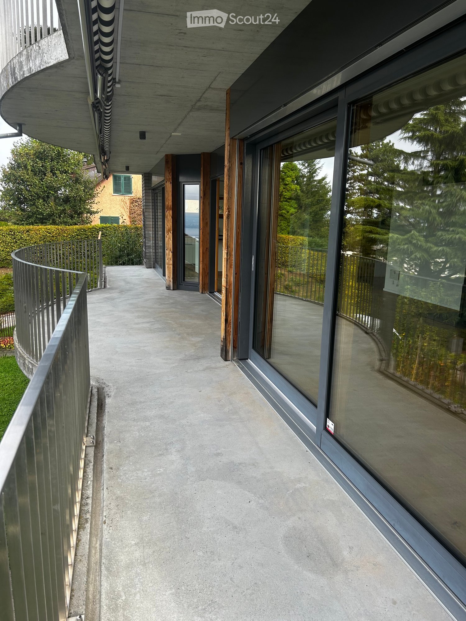 concrete floor, metal railings, sliding glass doors, trees, greenery, buildings