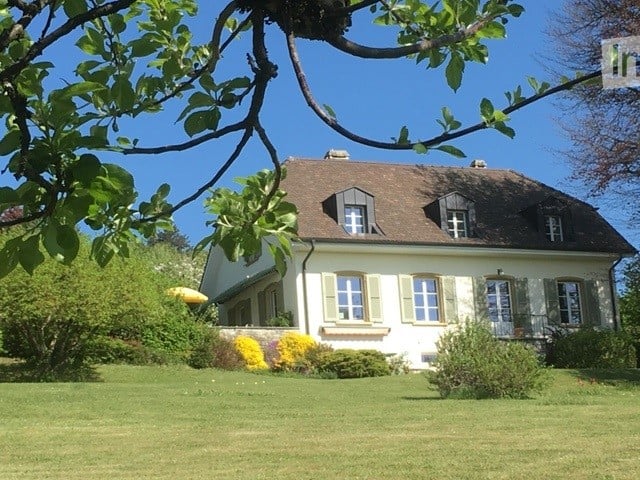 2 story house, brown roof, white walls, large yard, trees, flowers