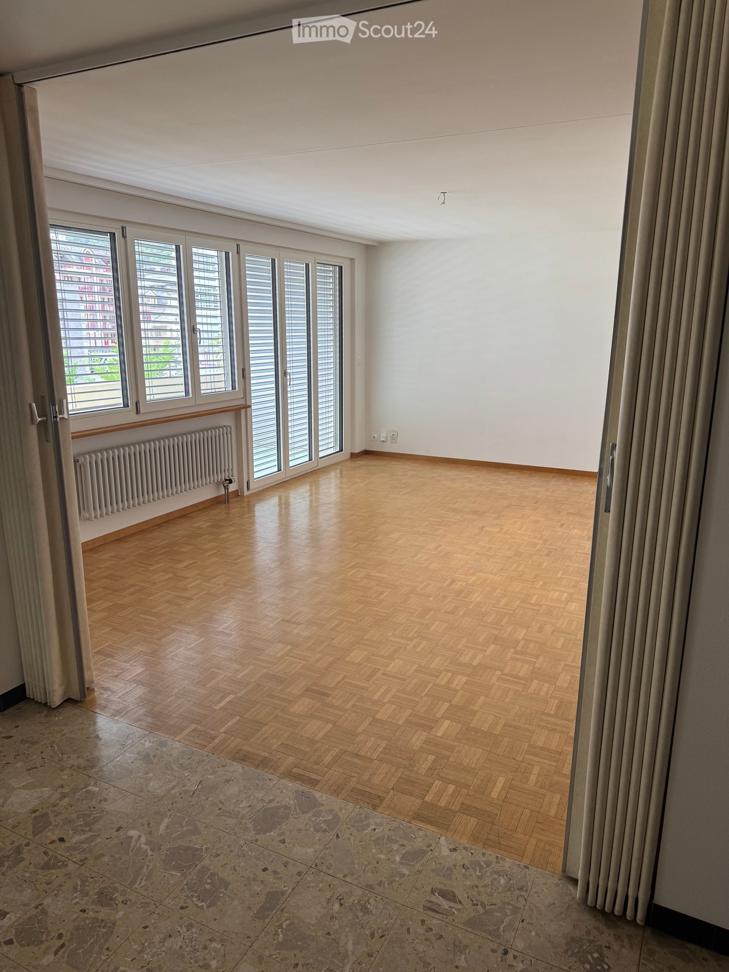large empty room, sliding doors, wooden parquet flooring, large glass windows, heating radiators