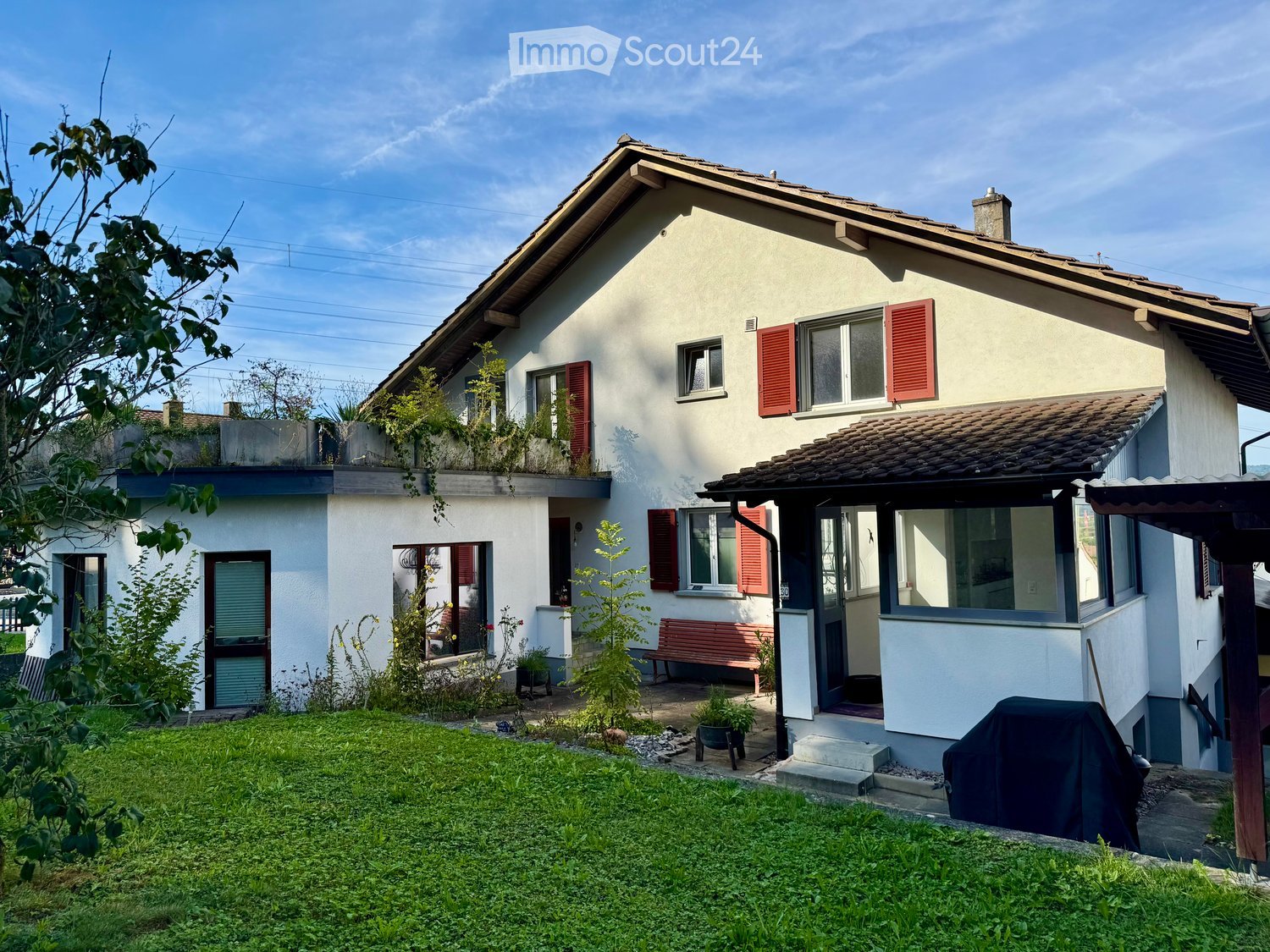Two story house, white walls, red shutters, covered front porch, garden, bench, BBQ cover
