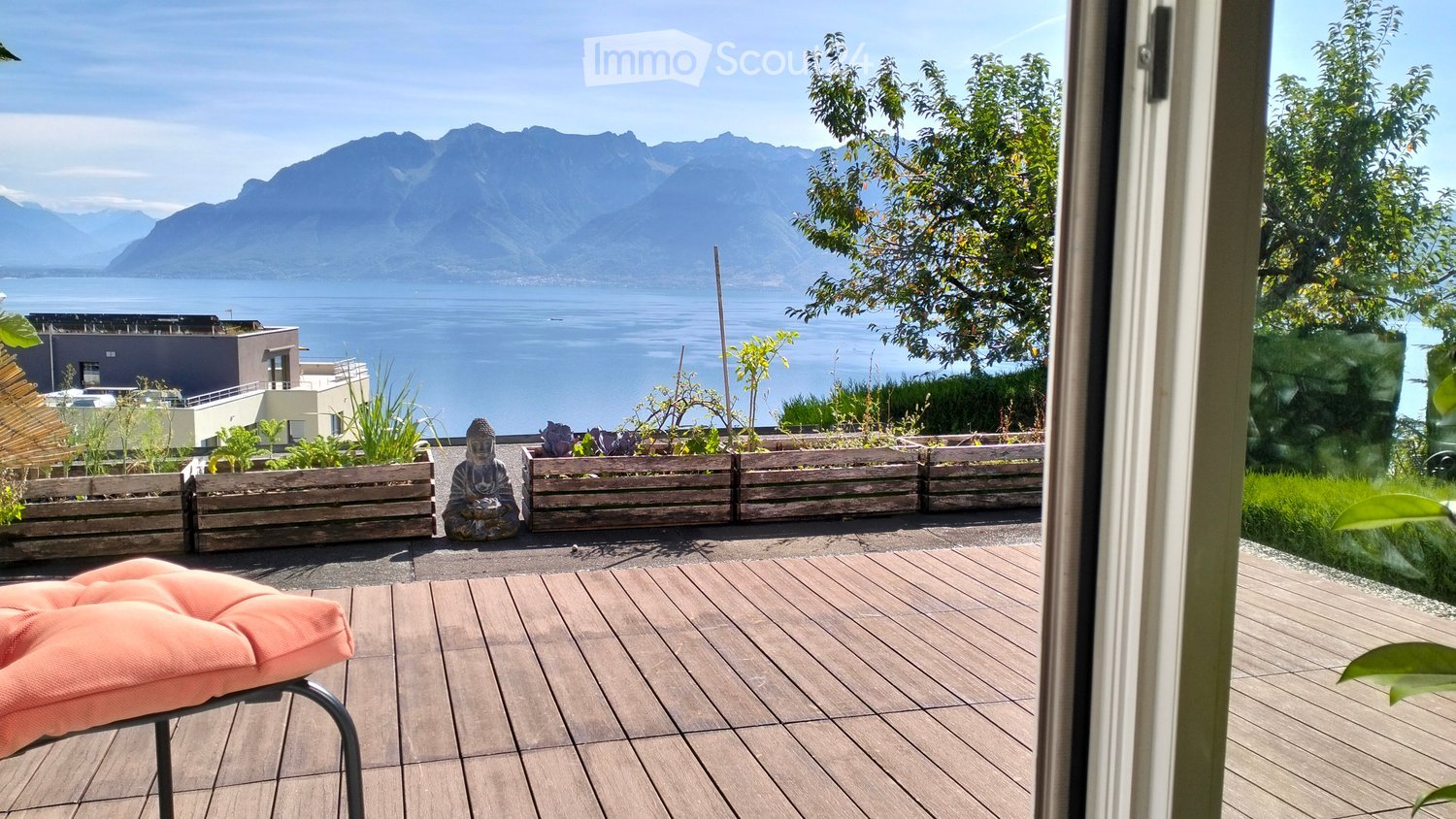 terrace, wooden floor, view of mountain and lake, several wooden planters with plants, pink cushion on chair