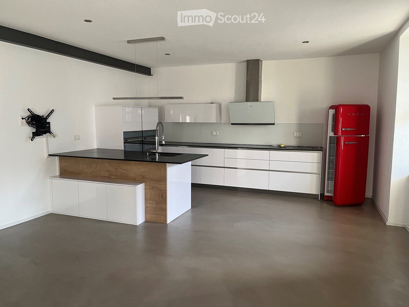 modern kitchen with central island, black countertop, white cabinetry, red refrigerator, under cabinet lighting, silver faucet