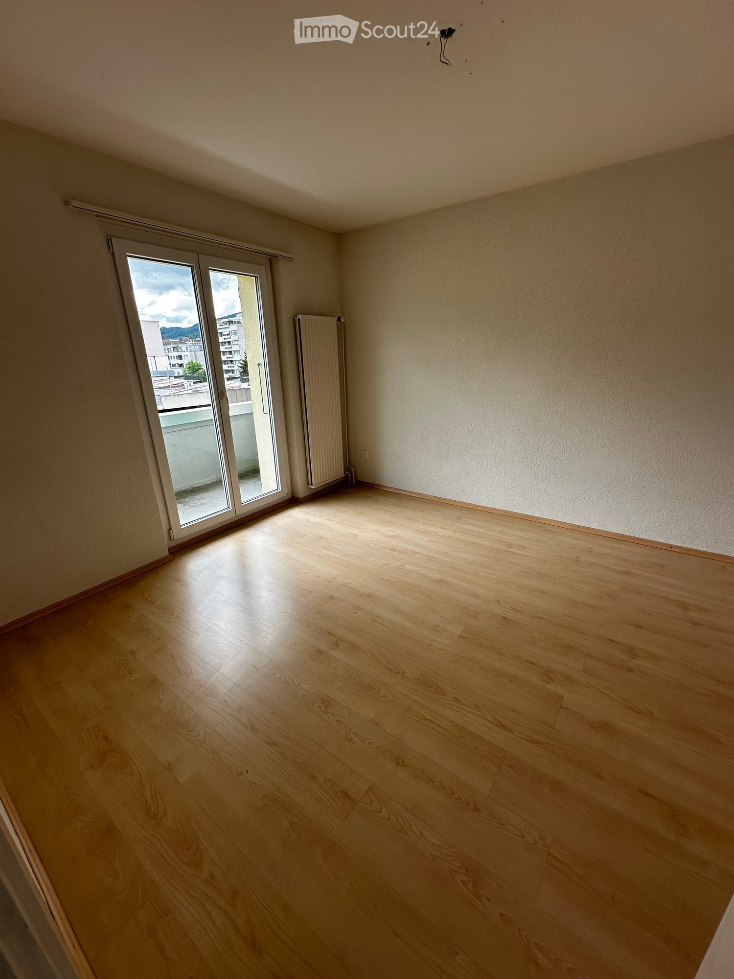 empty room with sliding glass door leading to balcony, wooden floor, white walls, radiator