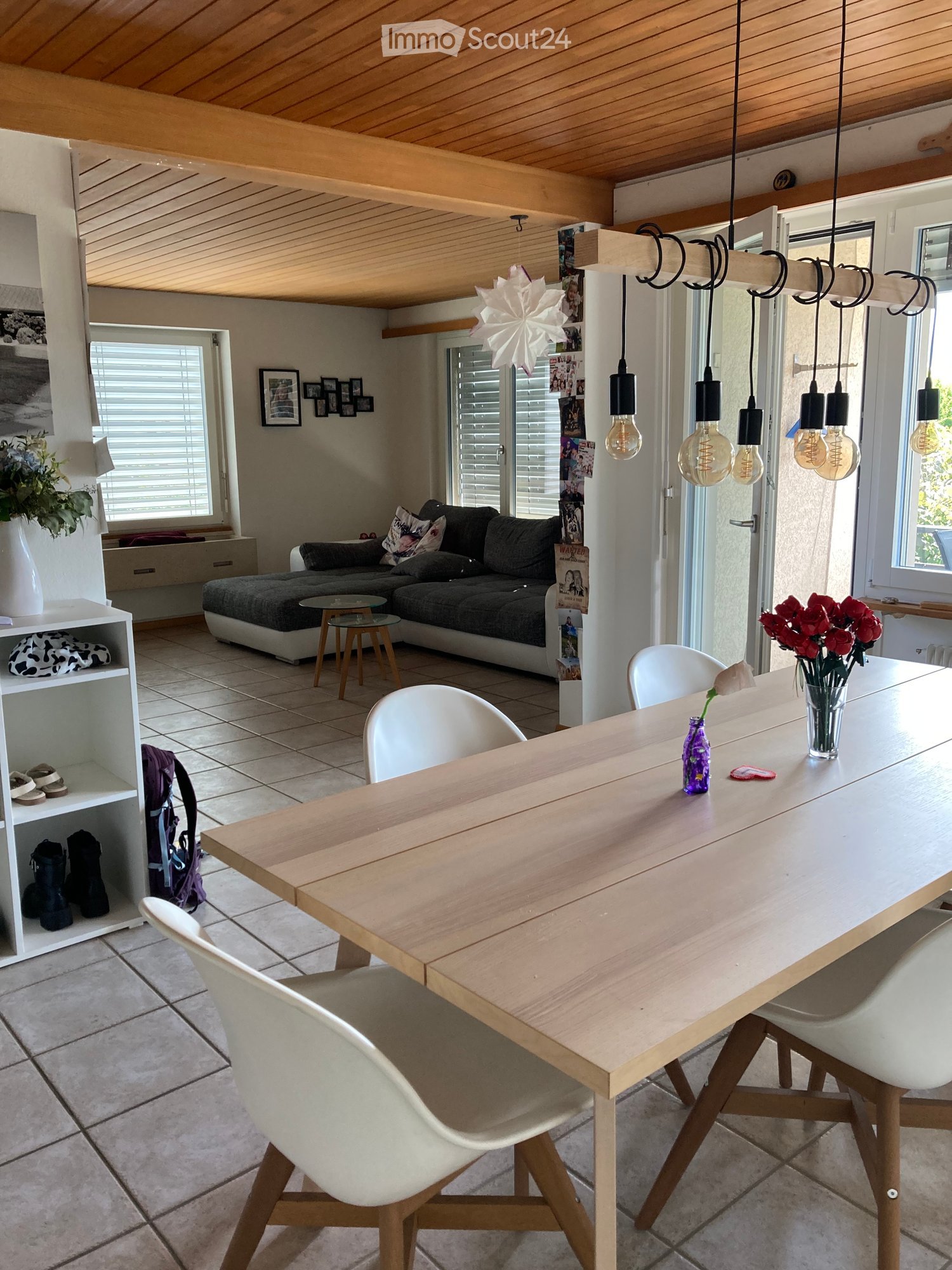 dining room, wooden table, 4 white chairs, pendant lamp, flowers on table, couch in living room