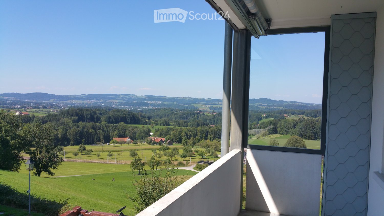 Balcony overlooking a lush green field and wooded hills in the distance