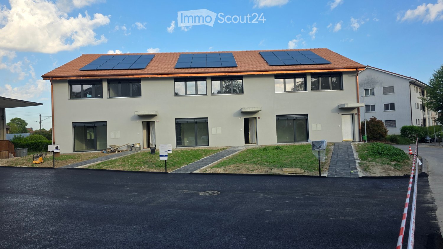 Two-story house with solar panels on the roof, large windows, and a paved driveway.