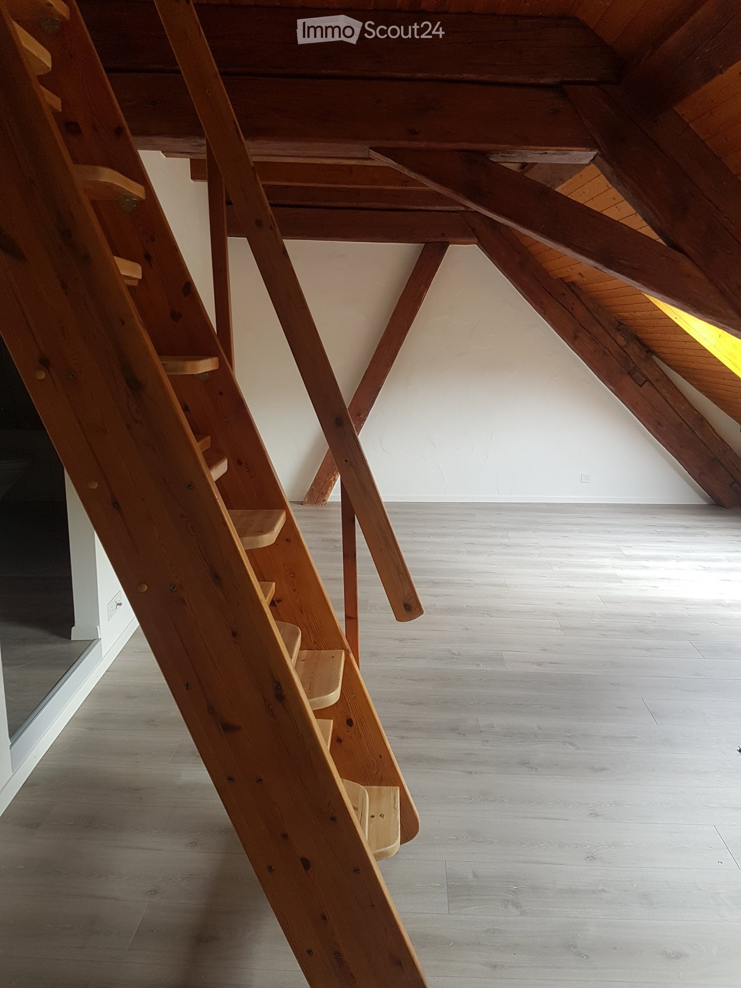 Empty attic room with wooden stairs and a sloping ceiling.