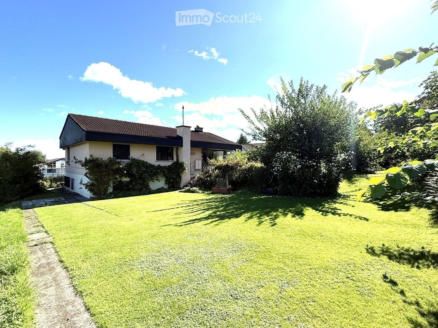 Detached house, two stories, brick exterior, brown roof, well-maintained garden with trees and shrubs, path leading to the entrance
