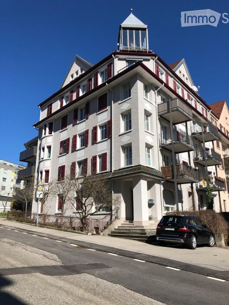 Multi-story building, red shutters, balcony on each floor, stairs leading to the entrance, small turret with glass walls