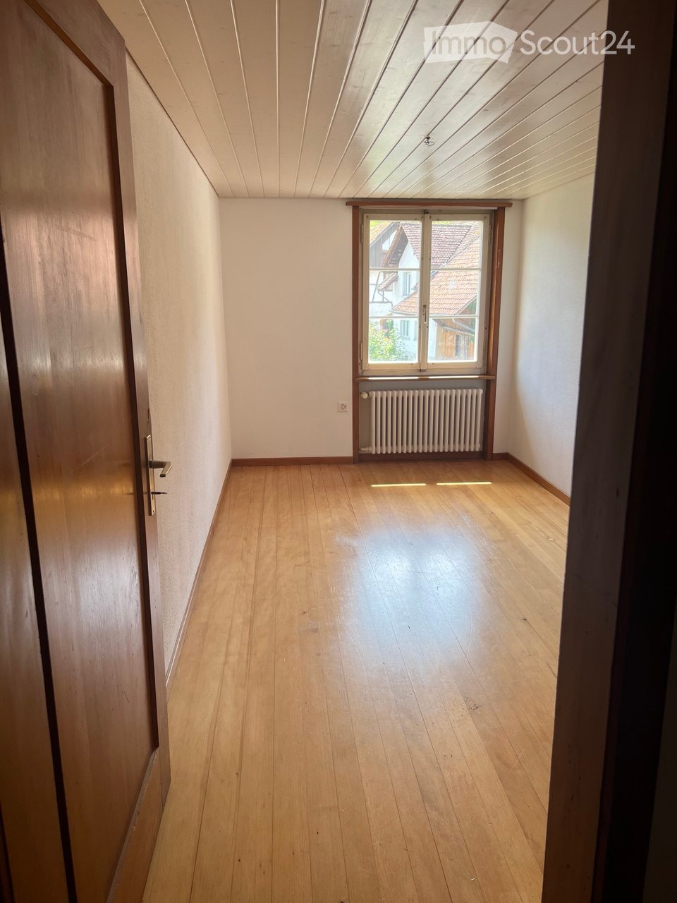Empty room with wooden floor and radiator. Window is large and sunny.