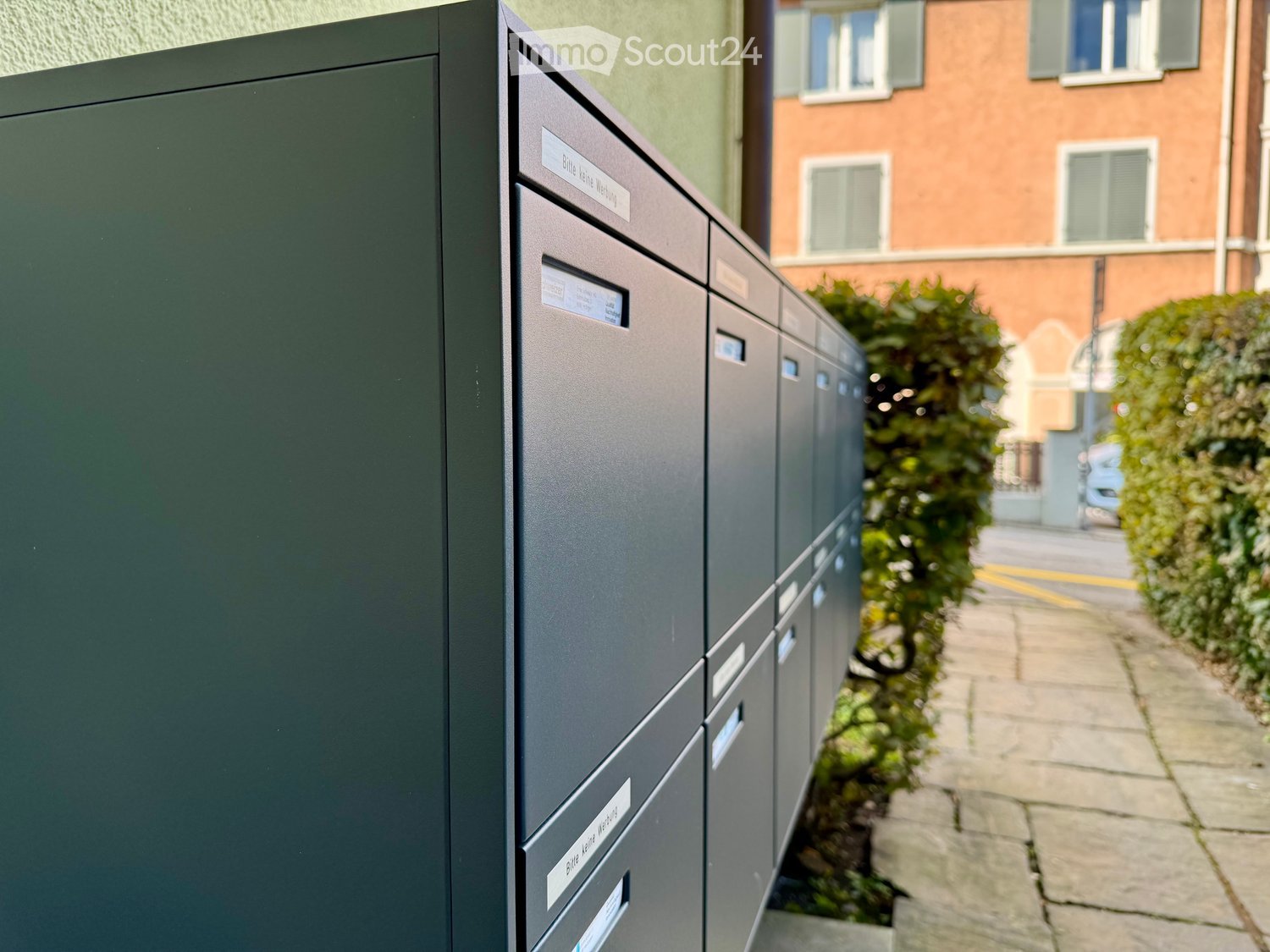 Green metallic mailboxes with labels and windows in the upper part, lined up on the street.