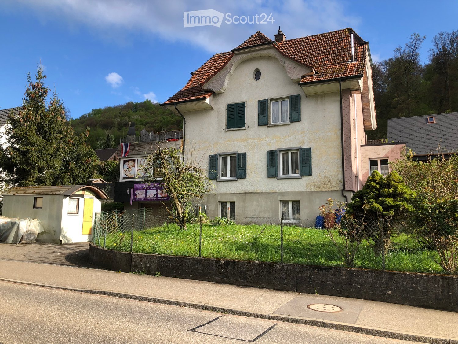 2-story building, white walls, red tiled roof, green shutters, grassy yard, small shed, fenced area