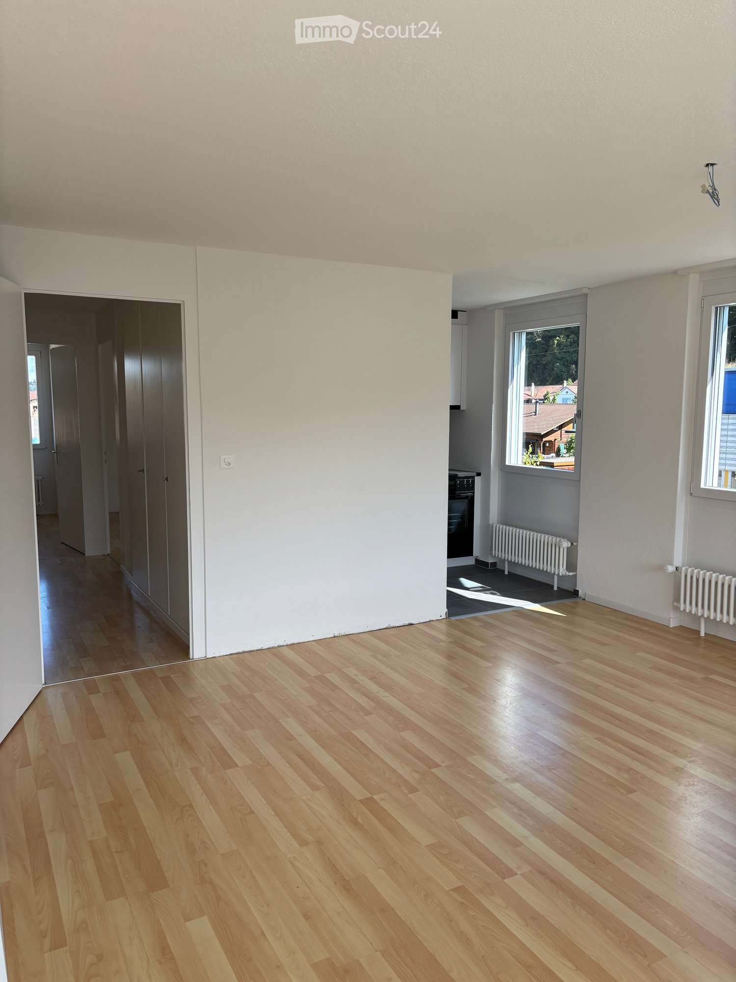 large room with hardwood floor, large windows, and open door to another room