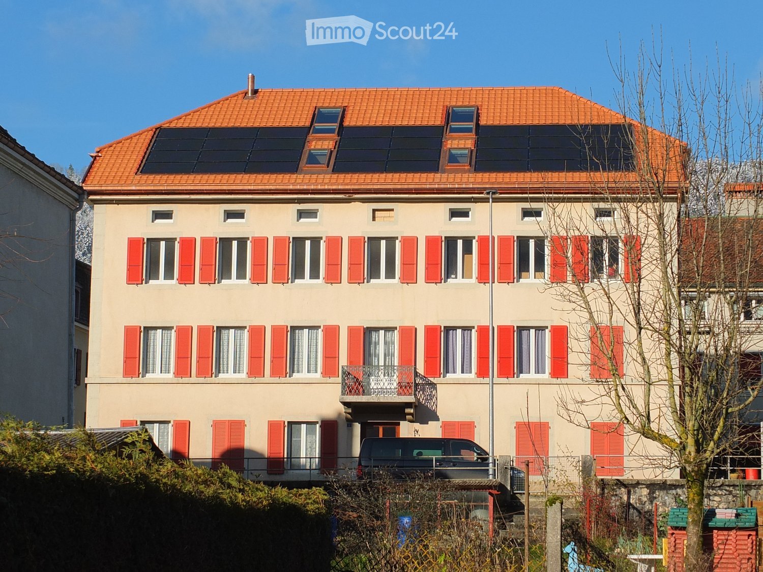 multi-story building, beige facade, red shutters, orange roof, solar panels, balcony