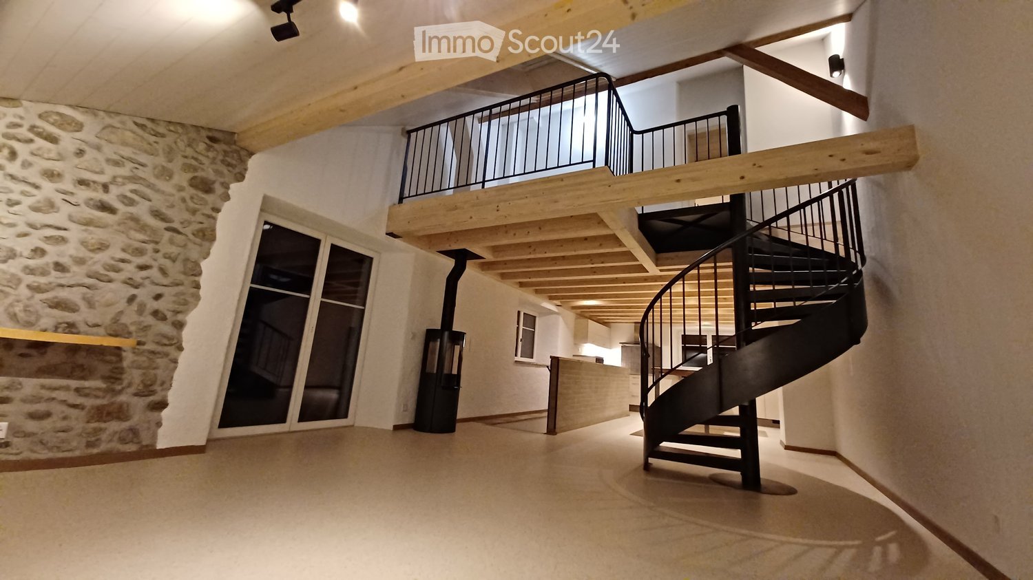 Open-plan interior with spiral staircase, wooden beams, stone wall, large windows, glass door