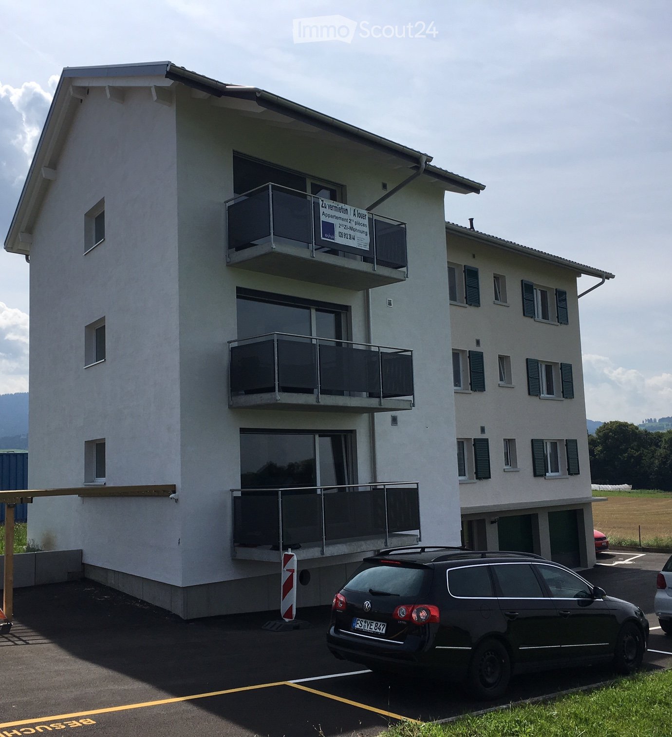 white apartment building, 3 levels, 3 balconies, one car parked