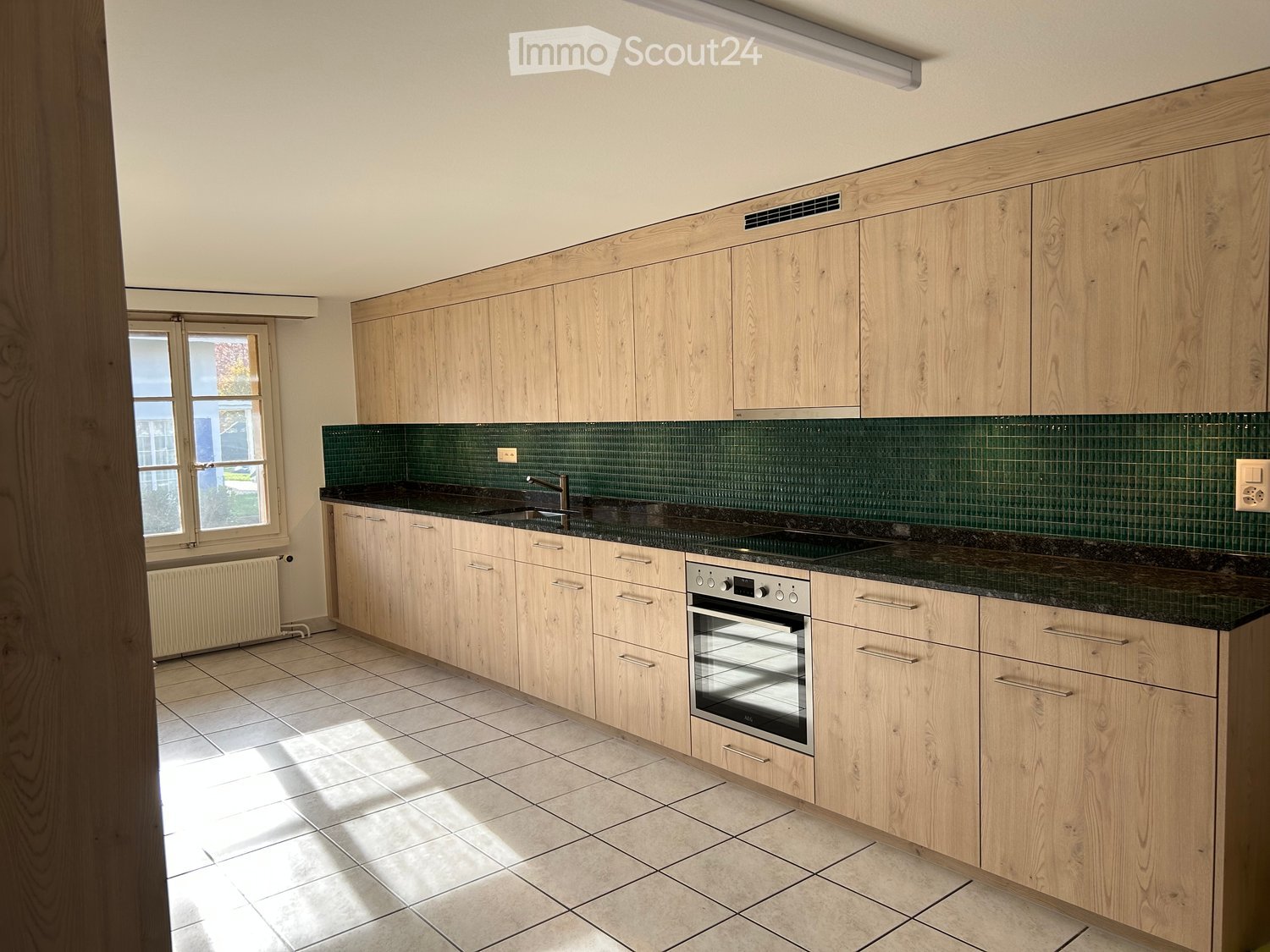 kitchen with modern cabinets, granite countertop, electric oven, sink with faucet, green backsplash tiles, underfloor heating, windows with views to outside, wooden floor