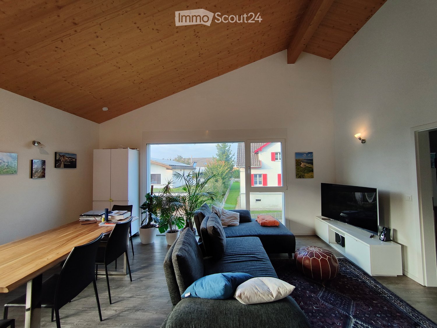 Large room with sofa, dining table, television, potted plants, white cabinets, decorative wall pictures, ceiling lights, carpet