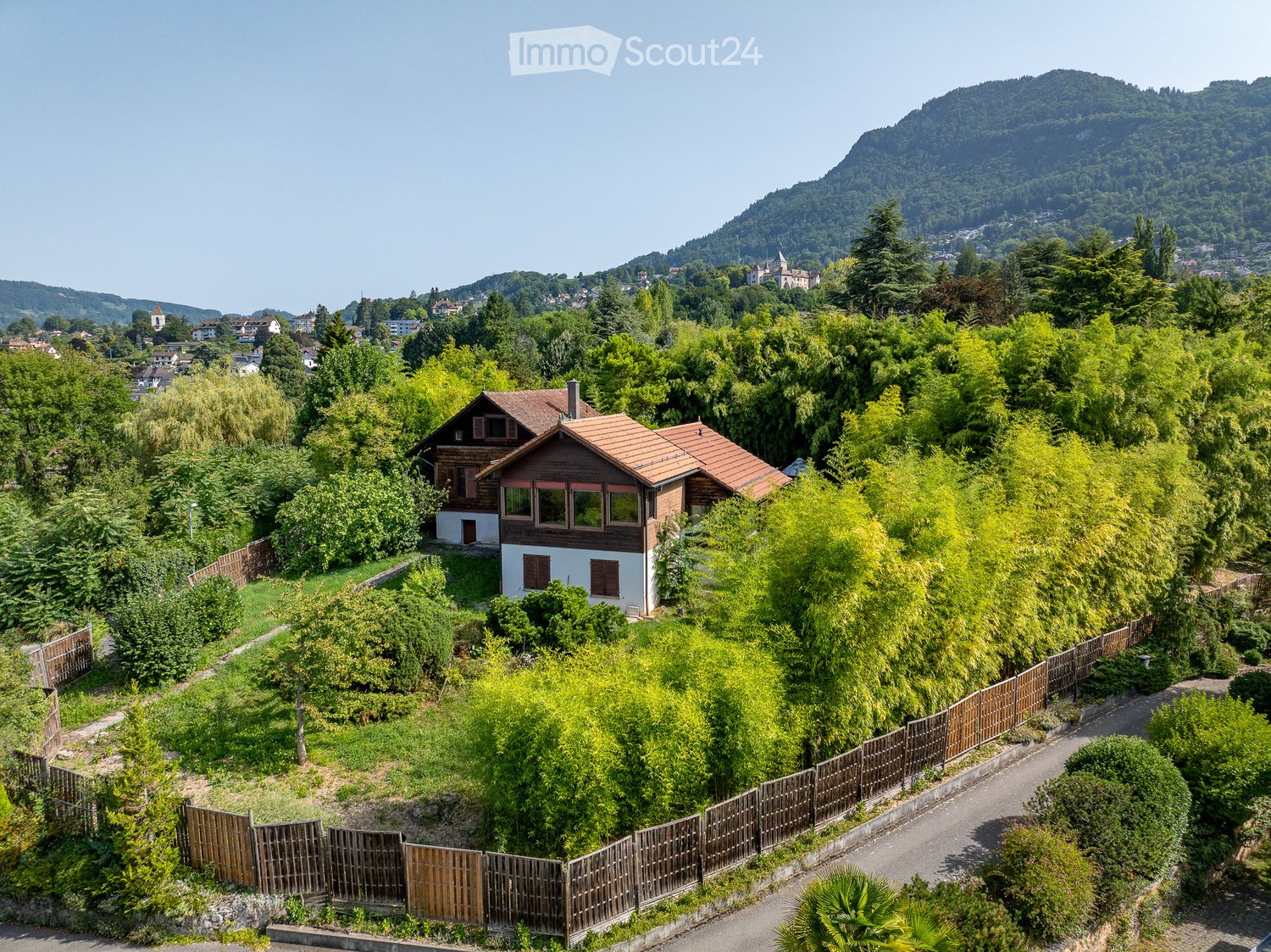 detached house with tiled roof, surrounded by green trees, situated in a scenic area with mountains