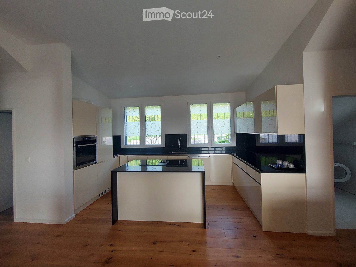 Modern kitchen, island, white cabinets, black countertops, stainless steel appliances, wooden floors