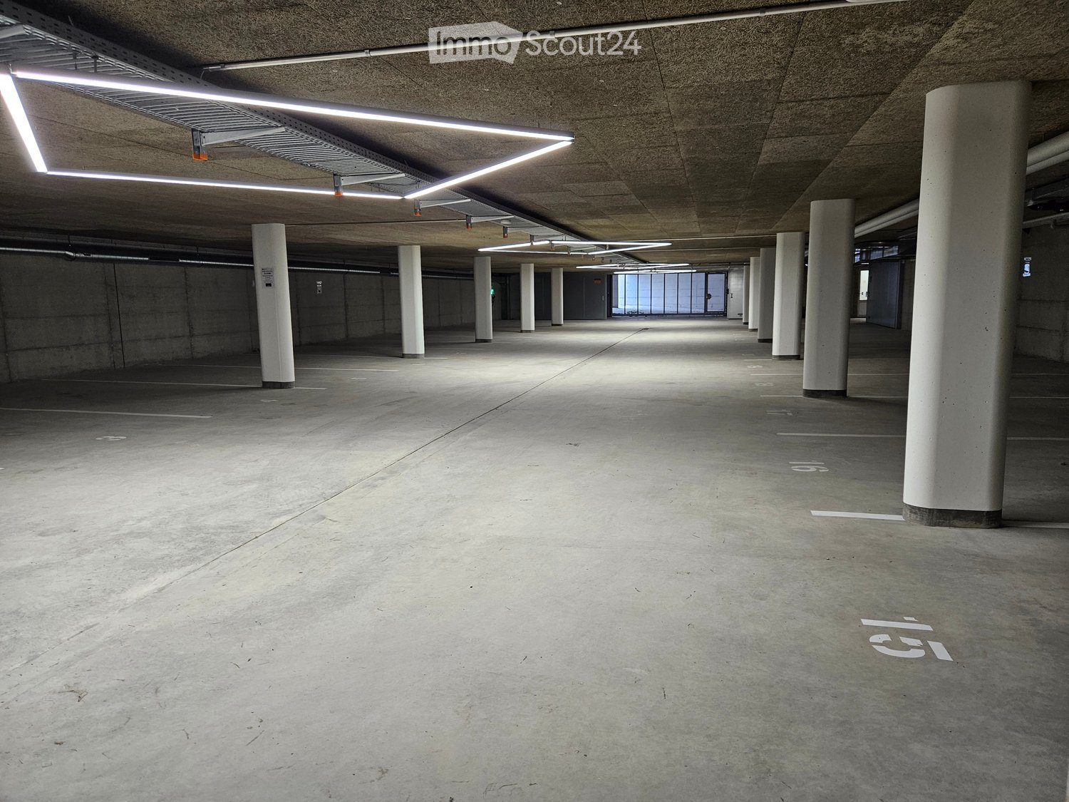 Underground parking space, square layout, illuminated by white ceiling lights, concrete floor, rows of vertical white pillars