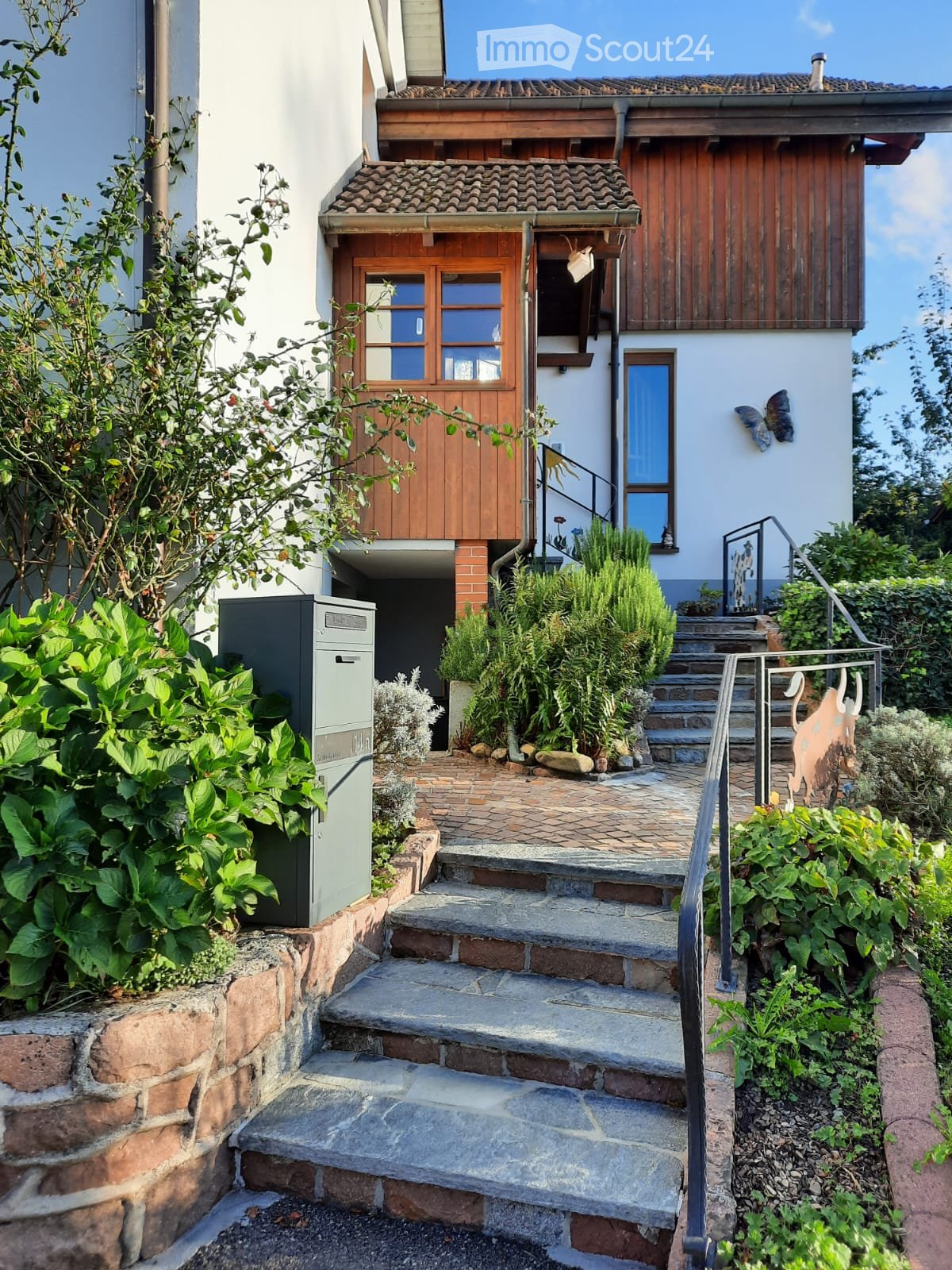 Two-story house with wooden wall on the top floor, staircase leading to the entrance, mailbox on the left side