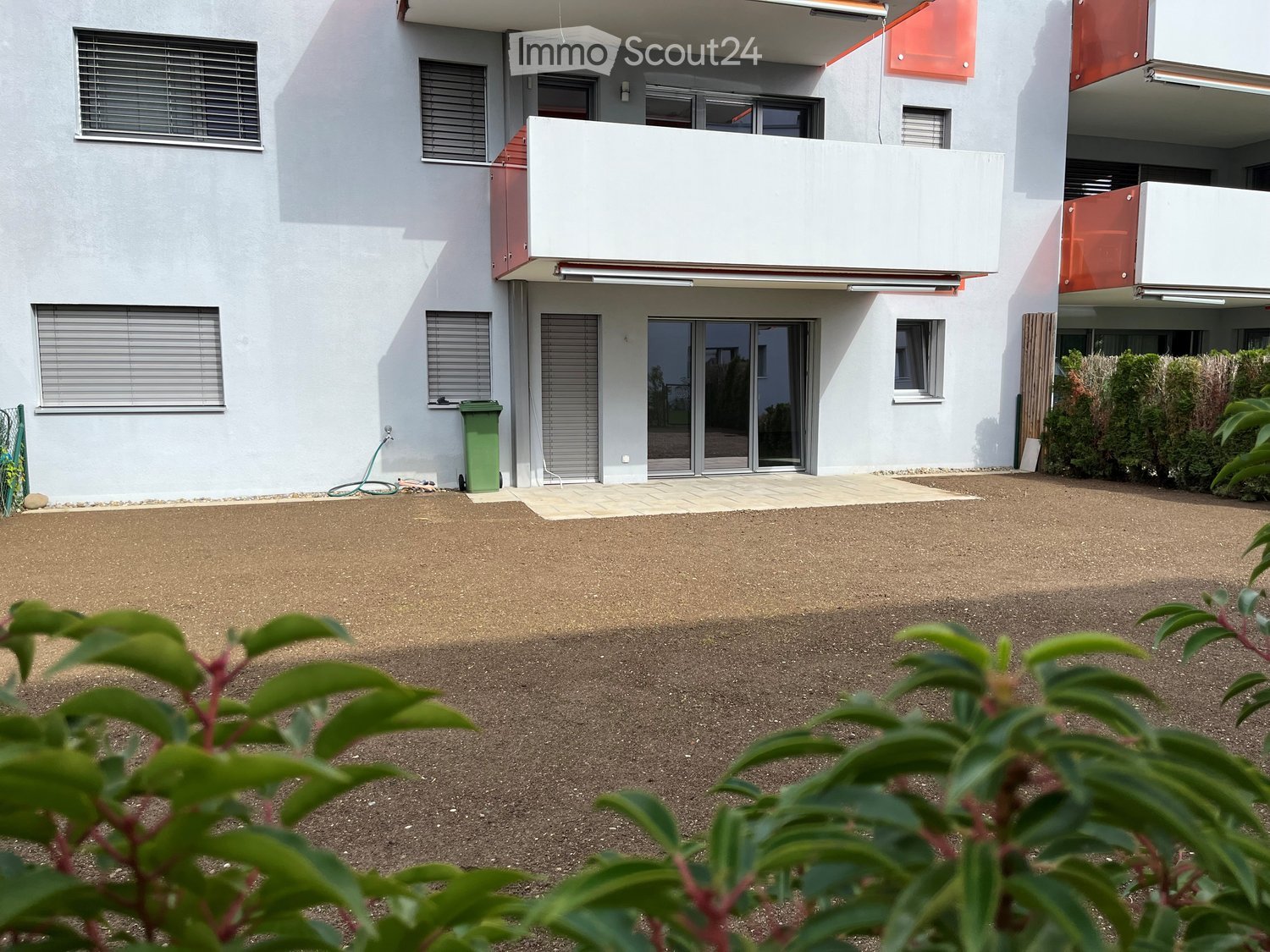 Apartment building, white walls, large glass doors, balcony, trash bin, hedge