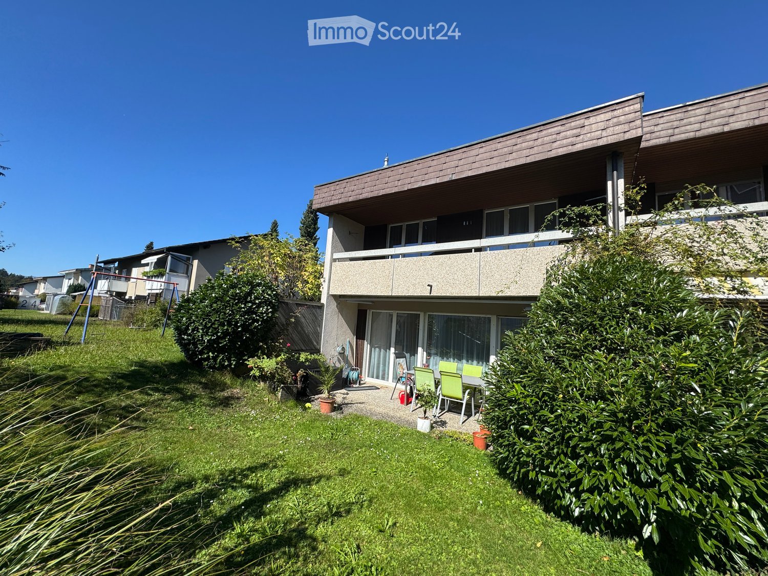 2 story house, brown facade, balcony, yard, greenery, garden furniture
