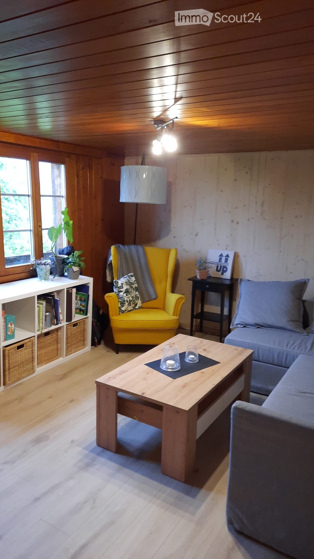 wooden living room with a large window, wooden coffee table, yellow armchair, blue sofa, bookshelf, potted plants