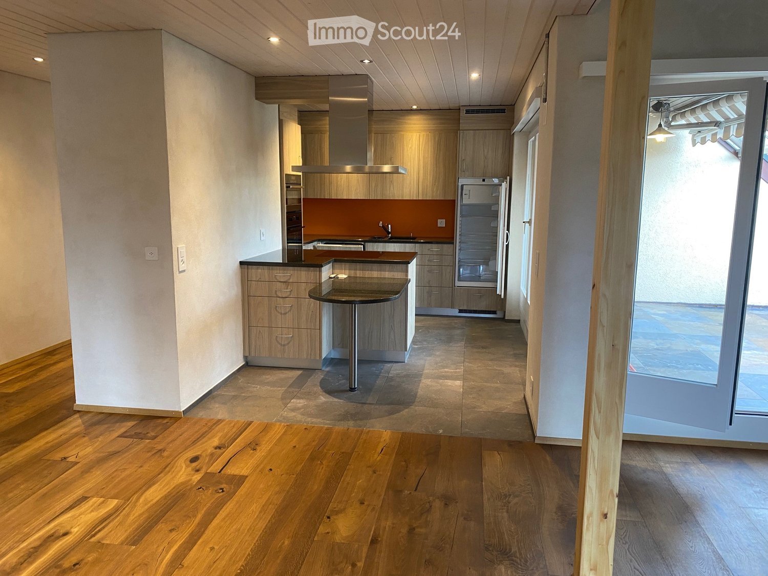 modern kitchen with wooden flooring, open shelving, large island, double sink, refrigerator, oven, range hood, white walls, balcony door, bright lighting