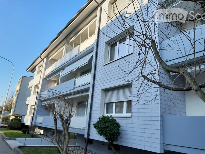 three-story building, blue brick exterior, multiple balconies, green shrubs