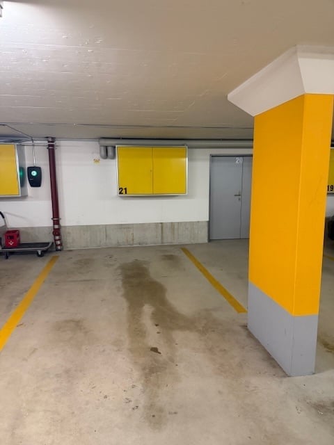 A vacant underground parking lot, yellow pillars, two yellow doors, two gray doors, two small yellow cabinets, gray parking space lines, and an entrance door to the left