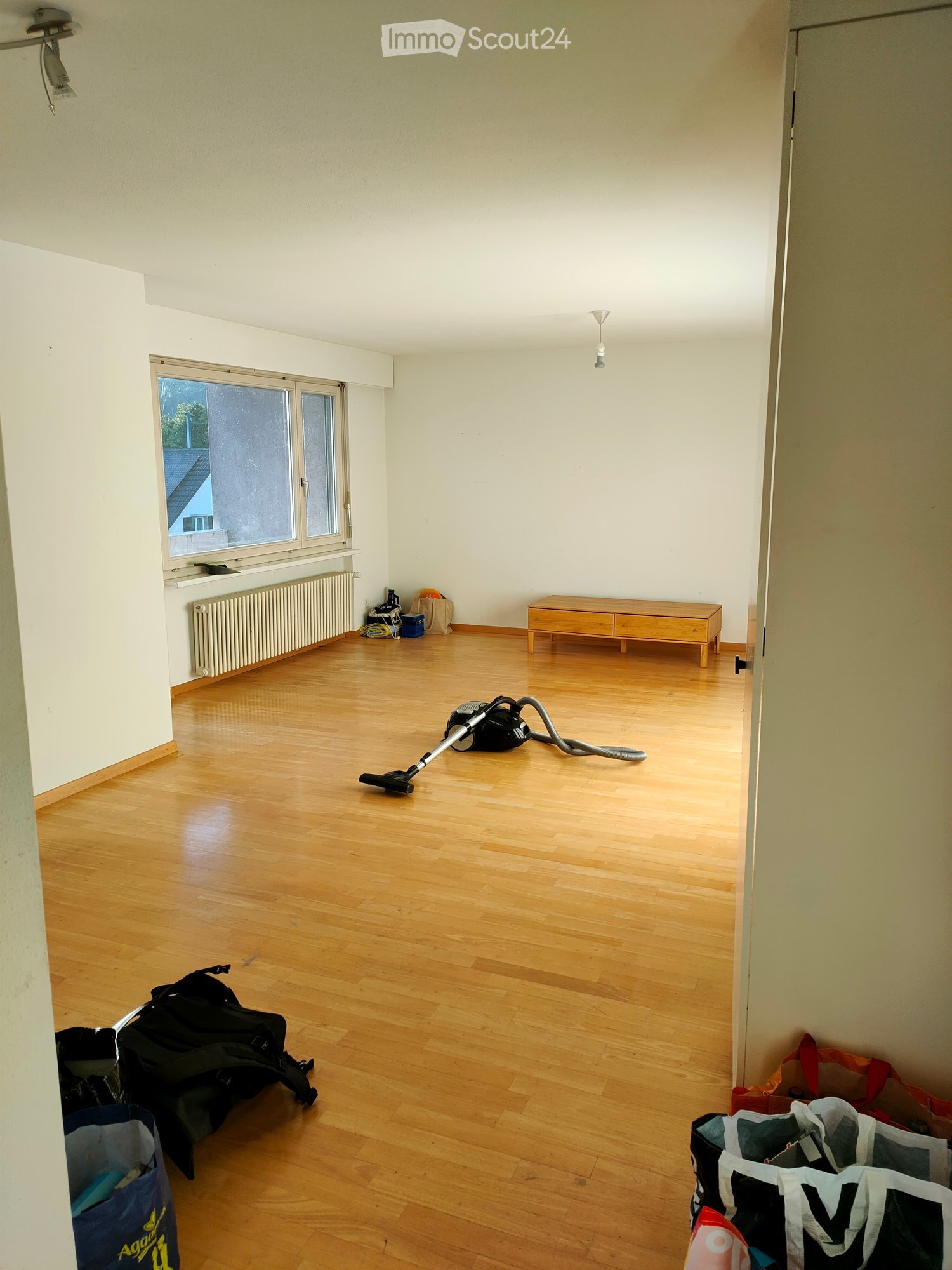 empty room, white walls, wooden floor, small window, heater, bench, vacuum cleaner
