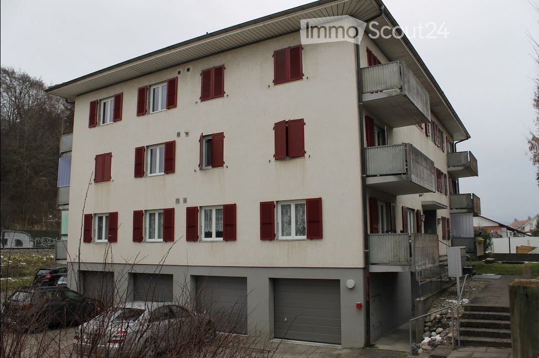 3-story apartment building, red shutters, white windows, multiple garages, concrete pathways, stairs to the entrance