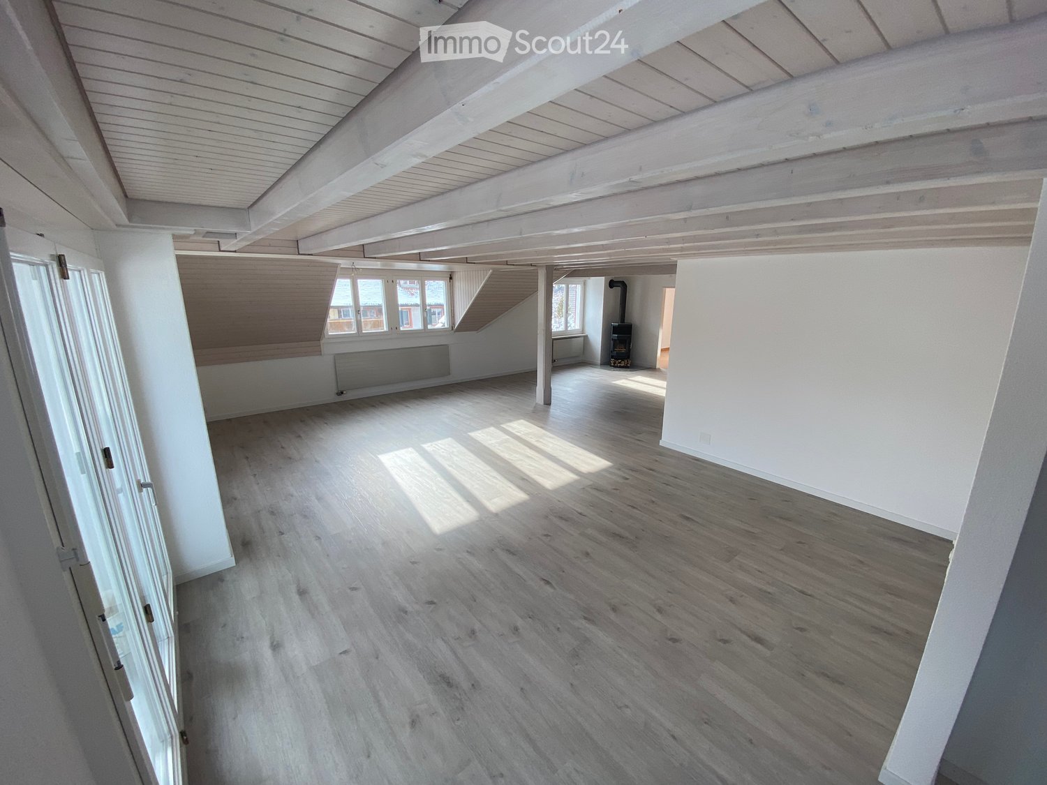 large room, wooden floor, white ceiling, white walls, large windows, fireplace, wooden beams, door