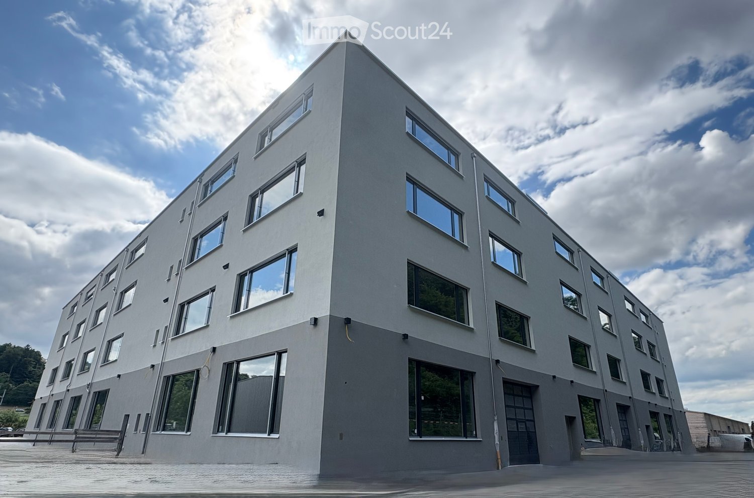 Large modern building with many windows, concrete ground floor, possible car parking area