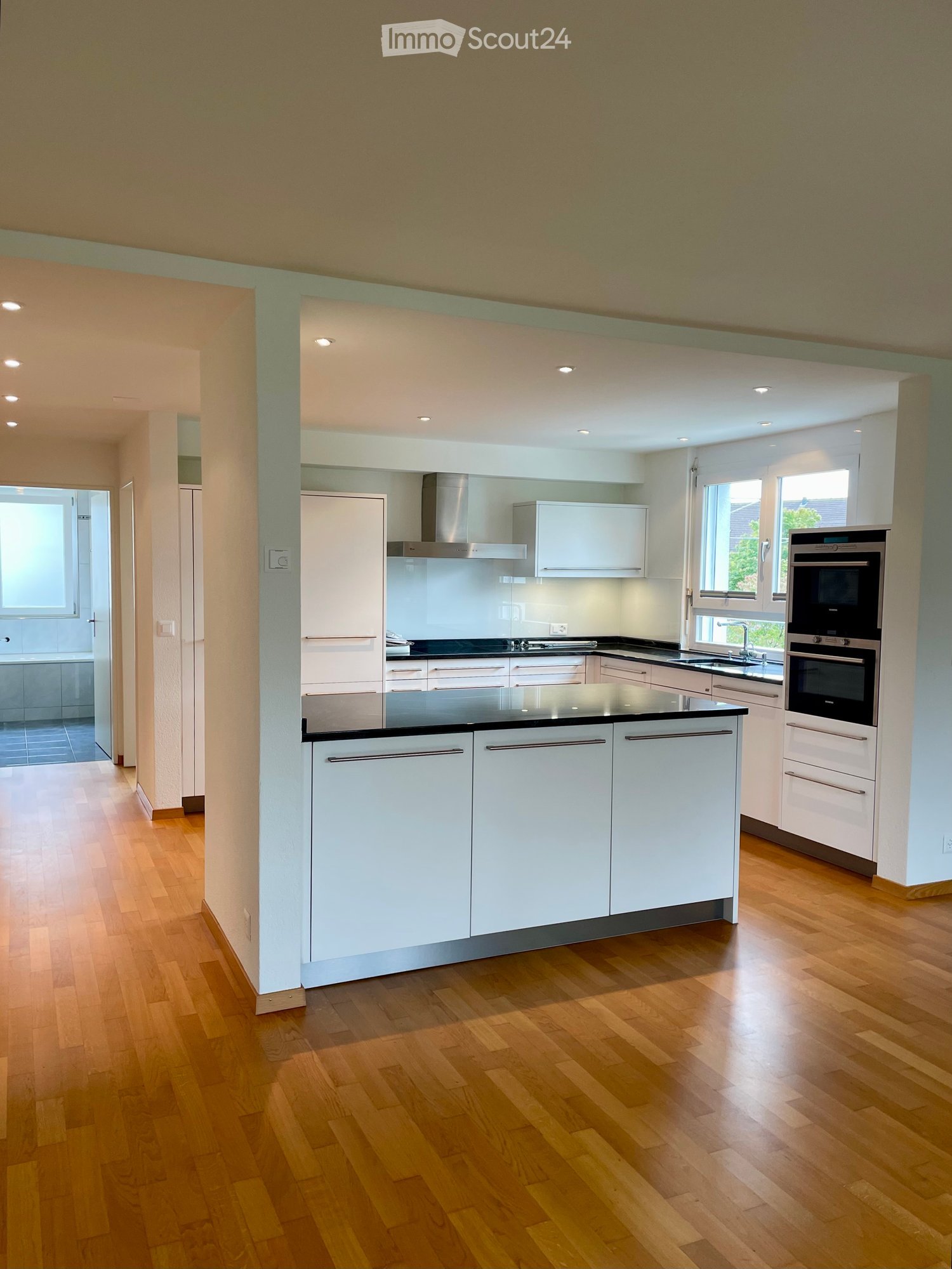 modern kitchen, island with black countertops, white cabinets, stainless steel hood and ovens, tiled flooring, central lighting