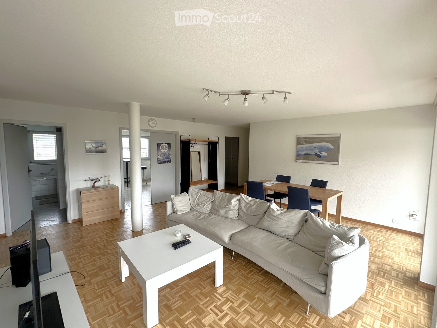 modern living room with hardwood floor, large white sofa, coffee table, dining table and chairs, framed pictures on wall